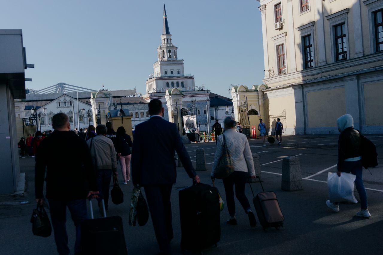 Tourists walking with luggage towards a historic building under a clear sky. Urban travel scene.